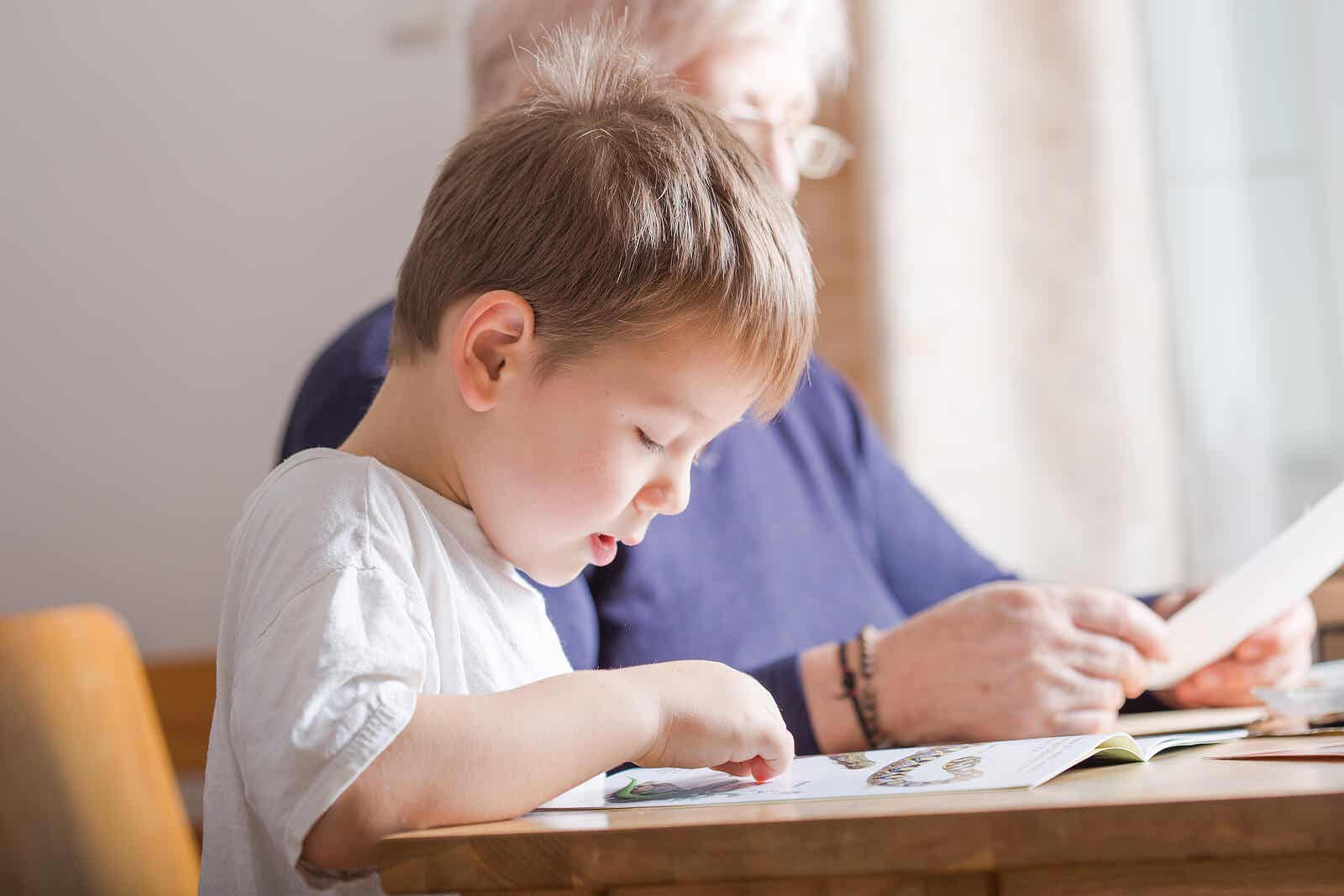 Et lille barn læser ved et bord ved siden af sin bedstemor