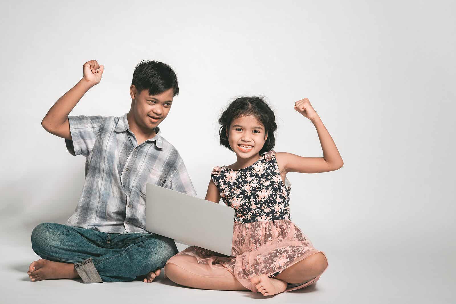 A child with down syndrome and his sister playing on a laptop and celebrating.