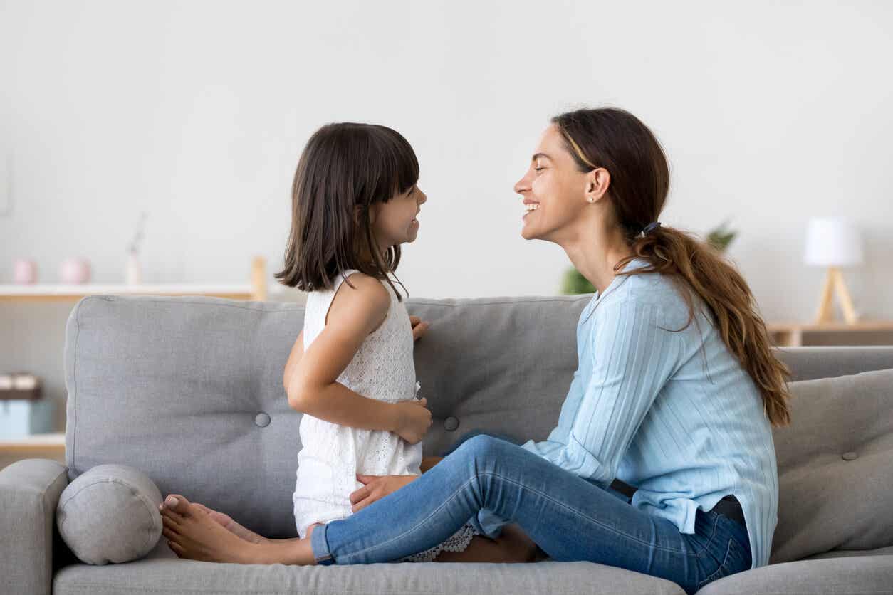 A mother sitting on the couch talking face-to-face with her young daughter.