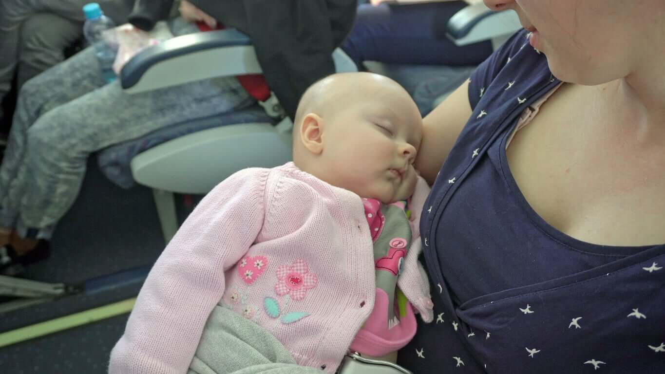 En mamma som håller sin sovande bebis på ett plan.