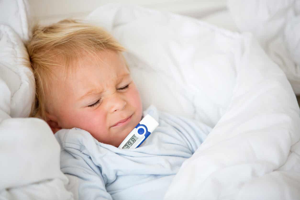 A toddler lying in bed uncomfortable, with a thermometer under his arm.