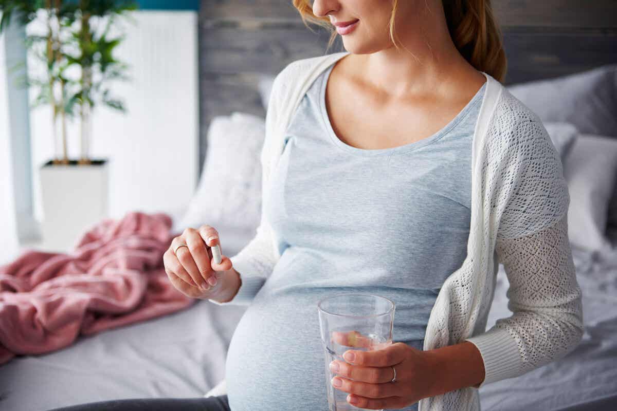 Kobieta w ciąży zażywająca pigułkę popijając szklanką wody.