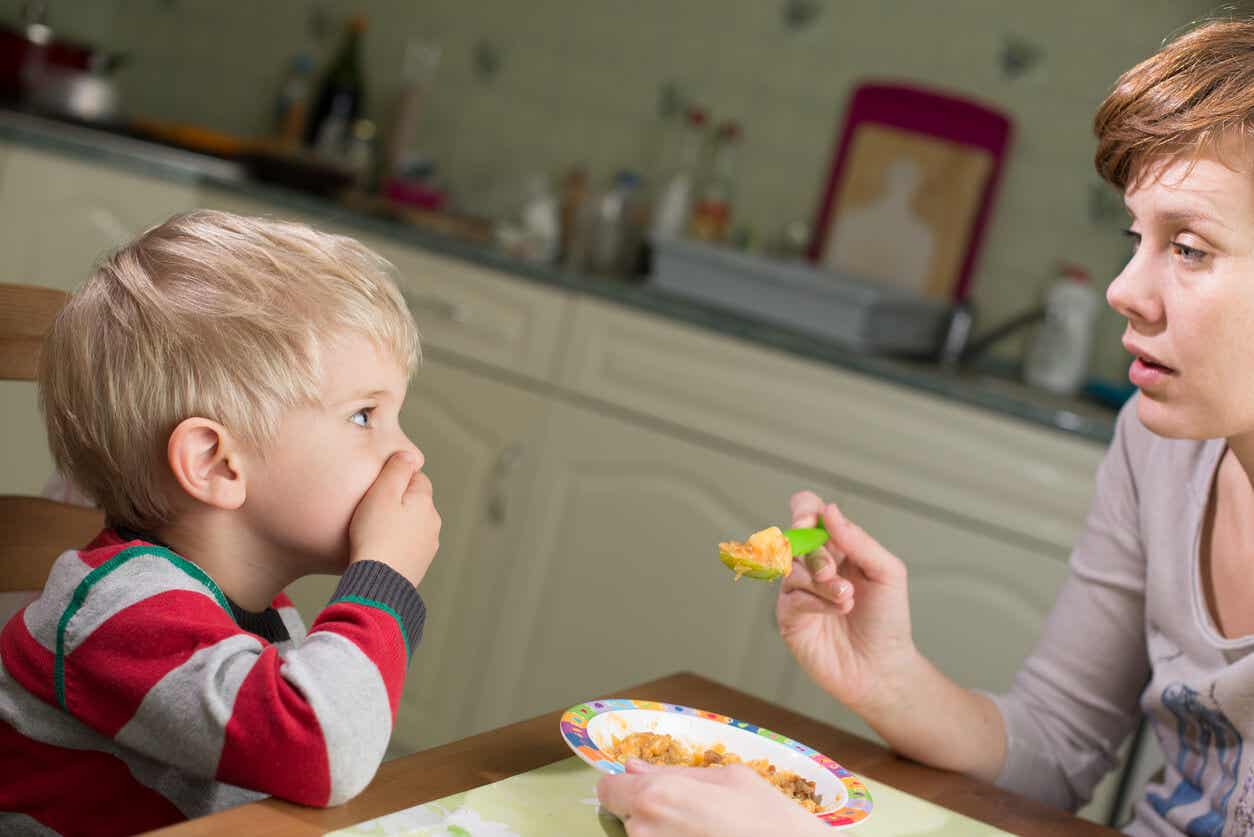 Een jong kind bedekt zijn mond terwijl zijn moeder hem probeert te voeden.