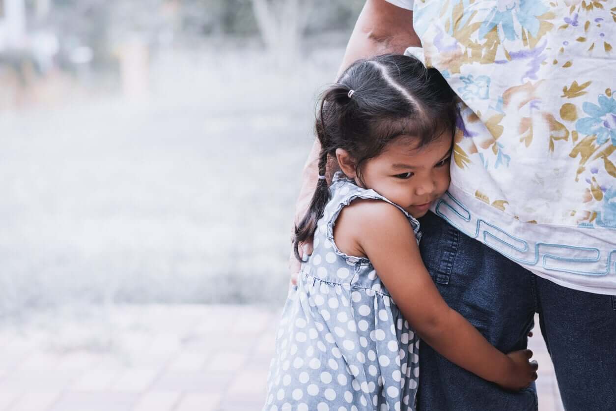 A young girl clinging to her father's leg.