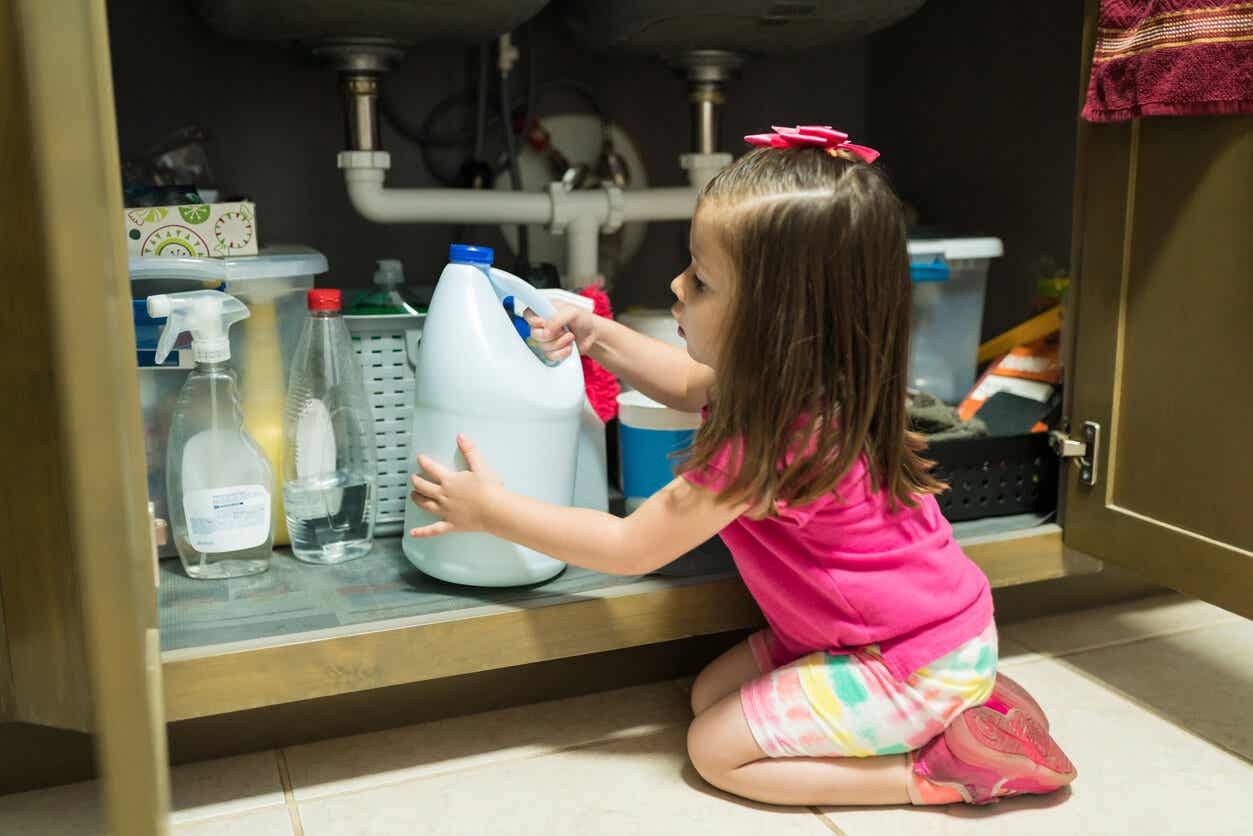 A toddler pulling a bottle of bleach from under the sink.