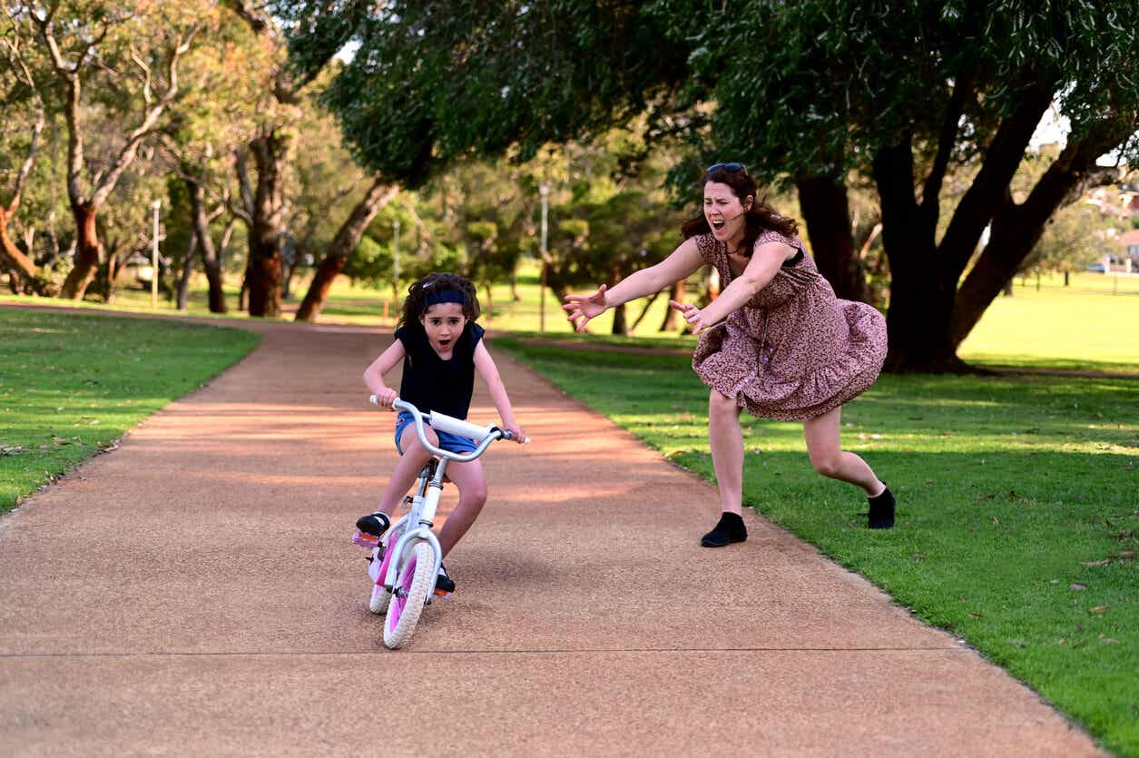 A mother running to help her daughter who's losing her balance on her bike.