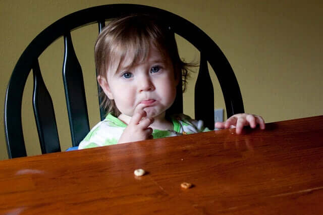 A toddler sitting at the dinner table looking stressed.