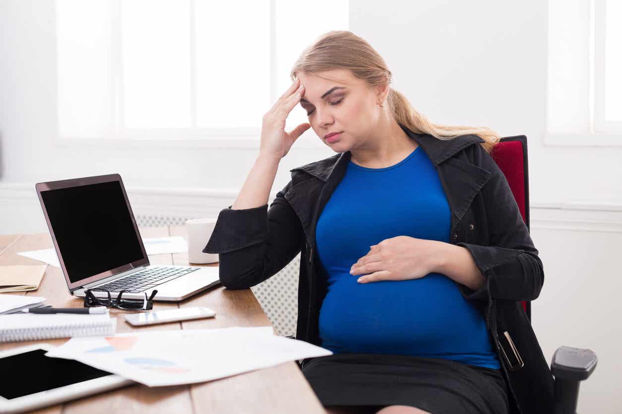 Een zwangere vrouw die op haar werk zit, haar voorhoofd strelend.