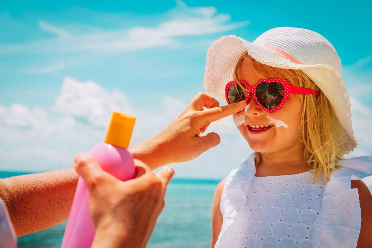 A mother applying sunscreen to her daughter's face at the beach.