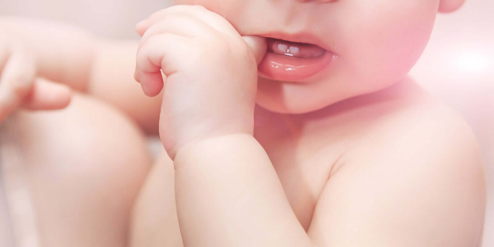 En baby som får tenner som tygger på fingeren.