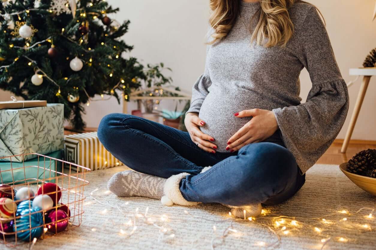 A pregnant woman sitting on the floor by the Christmas tree.