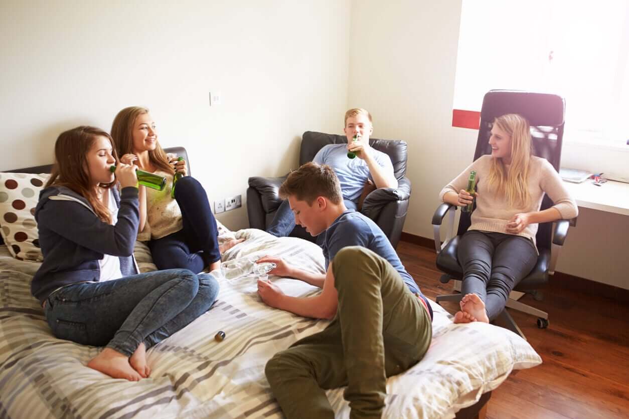 Teenagers hanging out in a bedroom drinking.