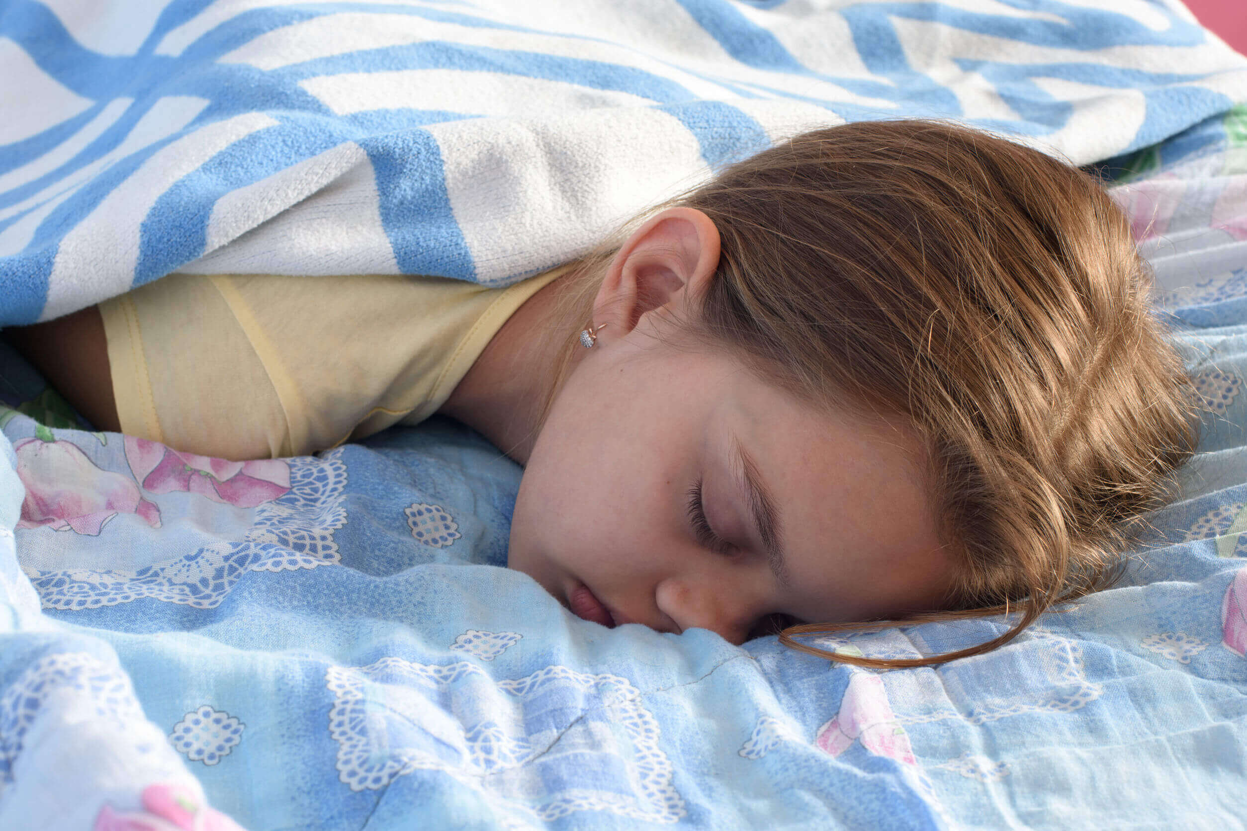 A teenage girl sleeping facedown on her bed.