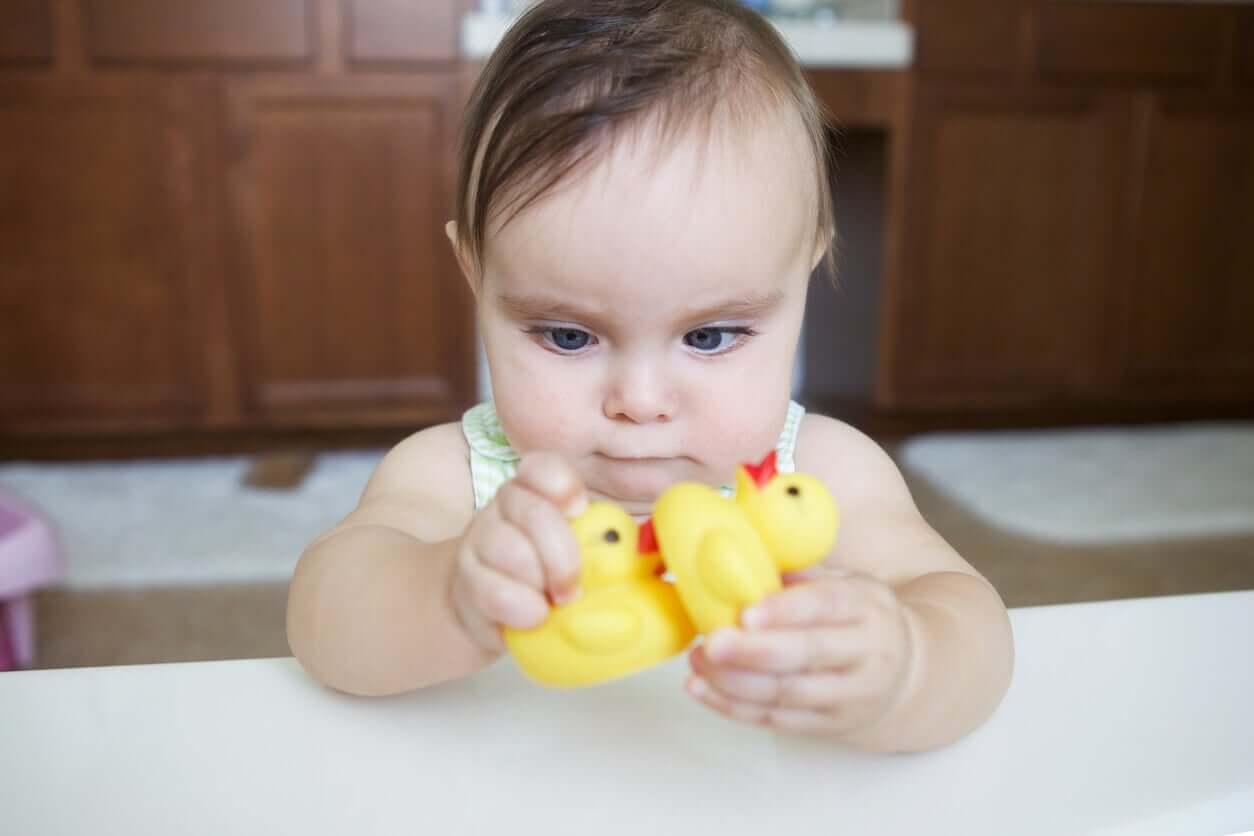 A baby with crossed eyes playing with rubber duckies.