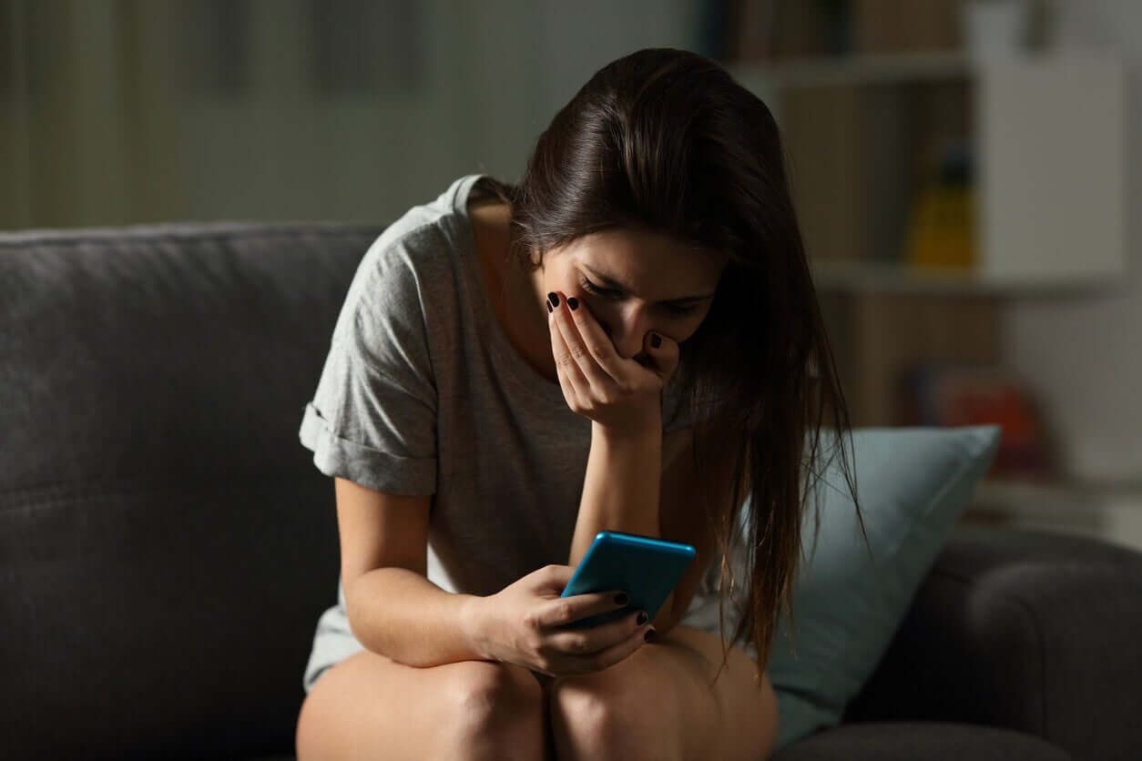 En tonåring tittar på hennes telefon med handen över munnen.