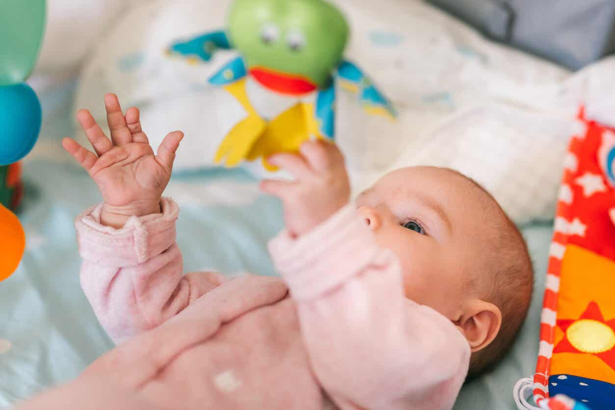 En flicka som ligger i en spjälsäng och leker med ett babygym.