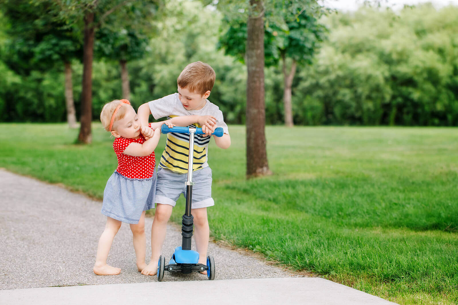 A boy and his little sister fighting over a scooter.