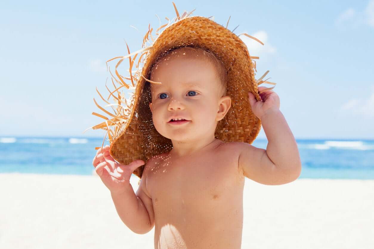 En baby på stranden iført en vevd halmhatt.