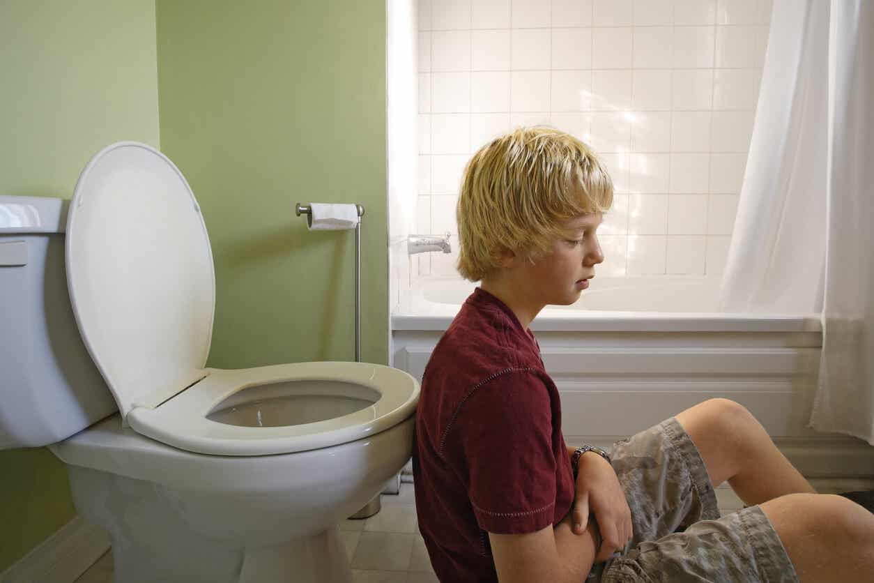 A teen sitting on the floor of the bathroom looking ill.