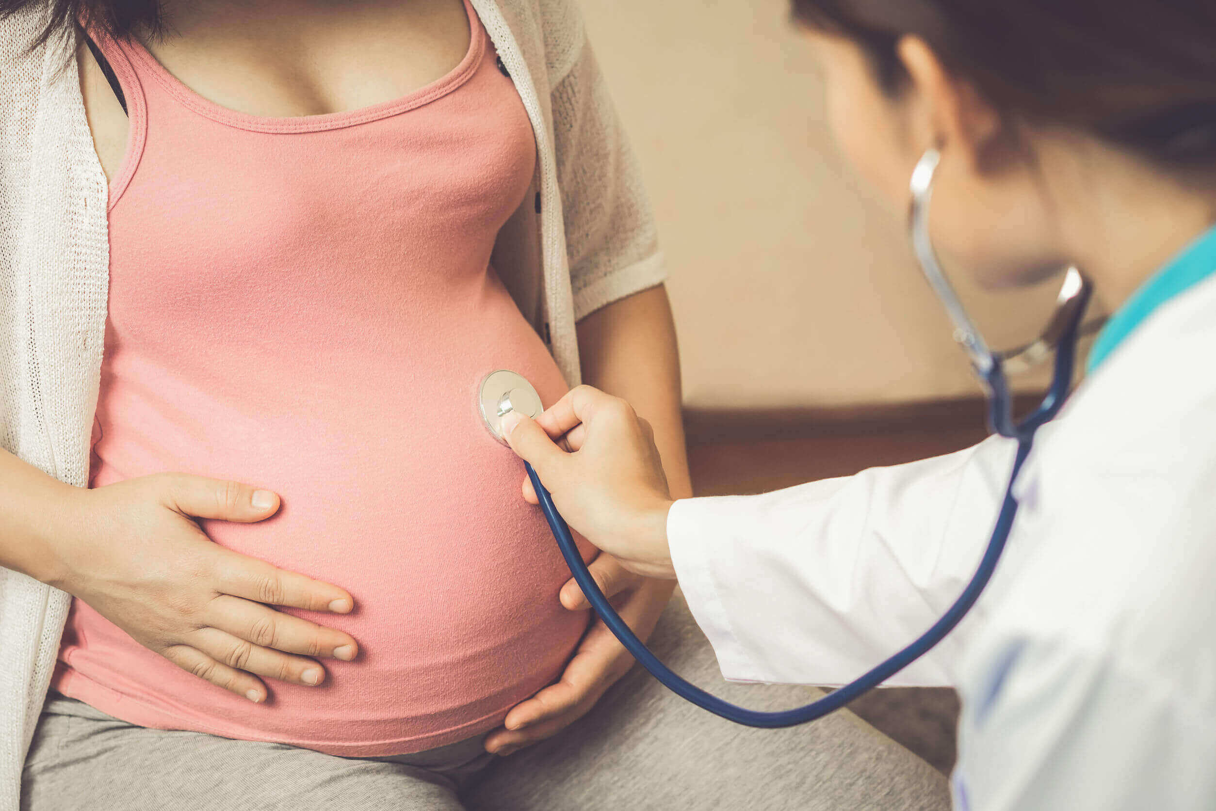 En läkare som lyssnar på en gravid kvinnas mage med ett steteskop.