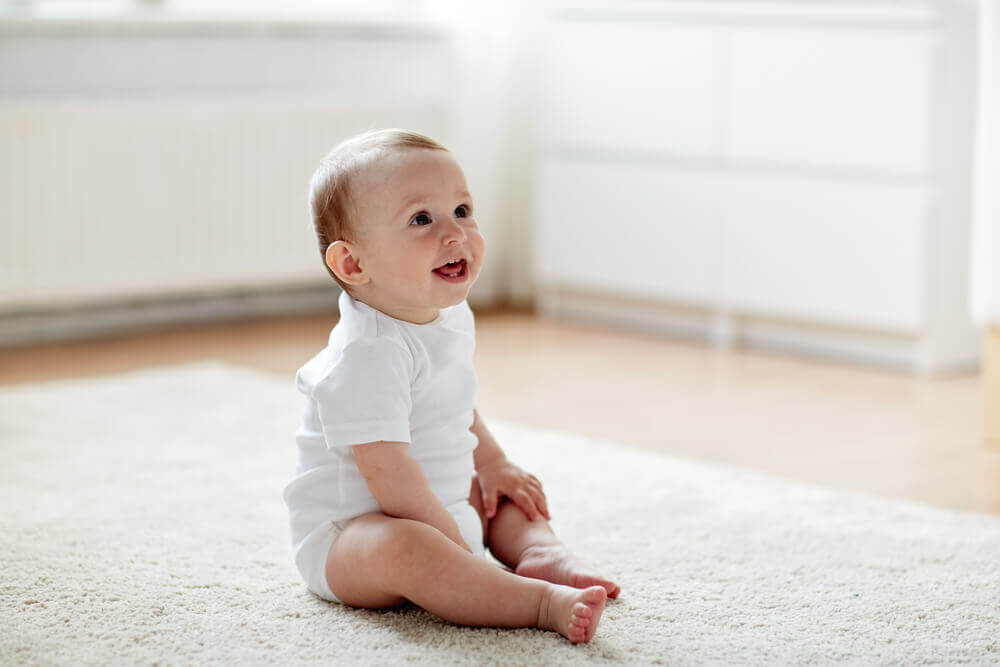 A happy baby sitting on the floor.