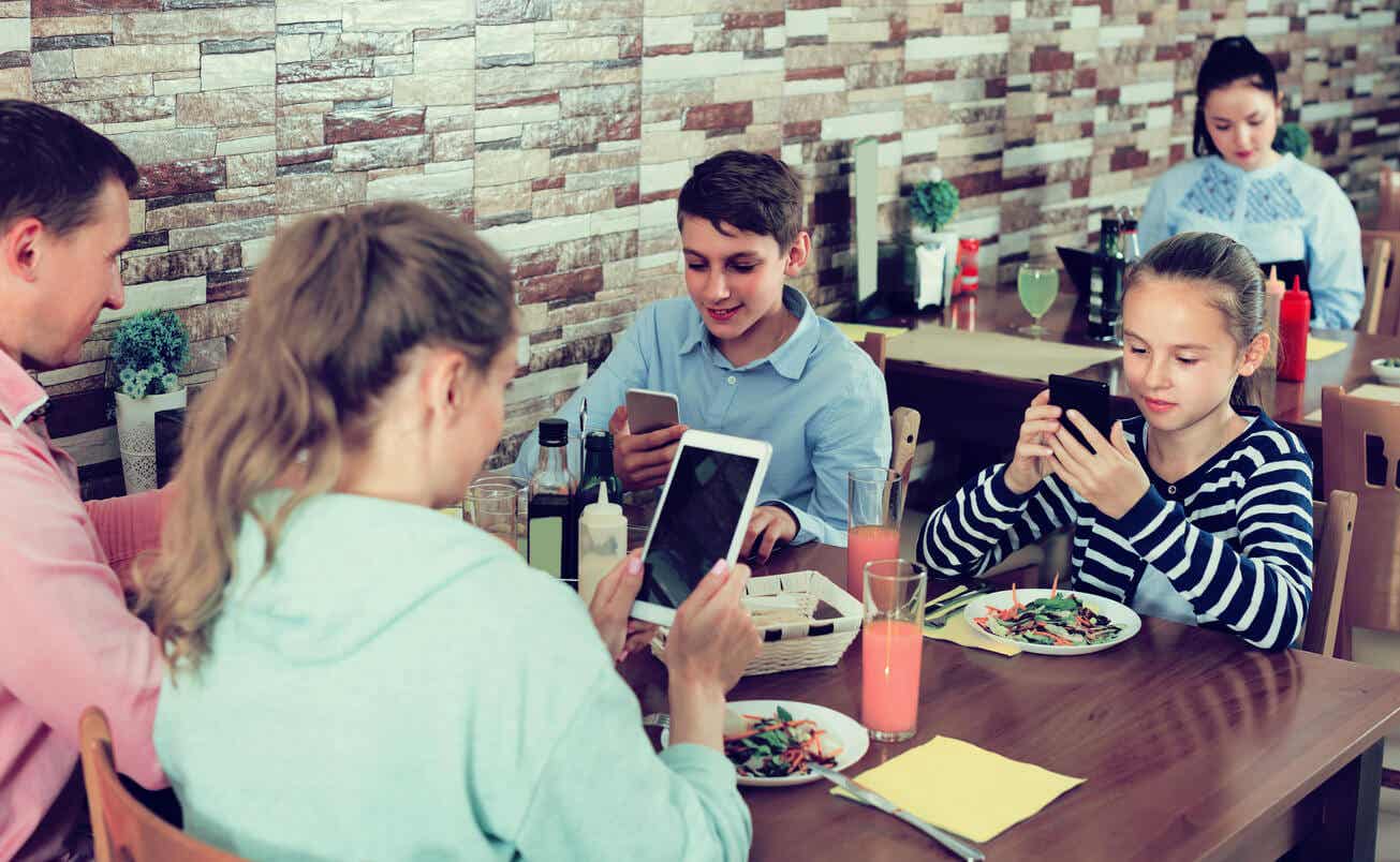 En familj ser på sina skärmar på en resturang.