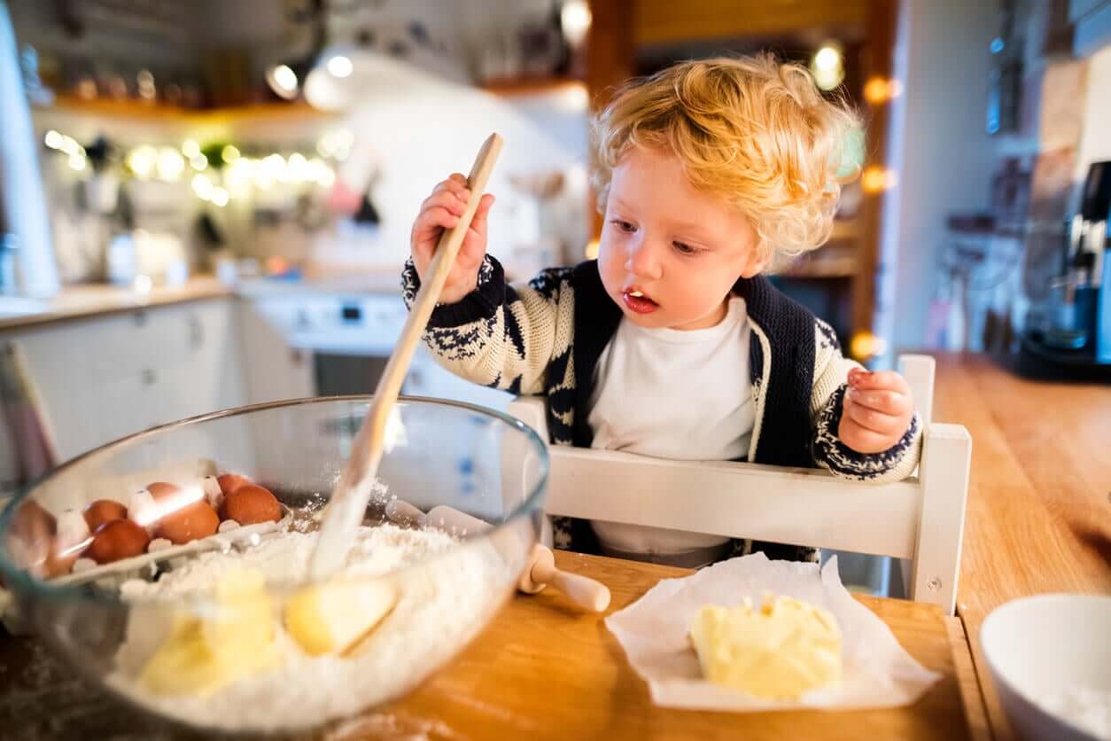 A toddler in a learning tower stirring a bowl of ingredients.