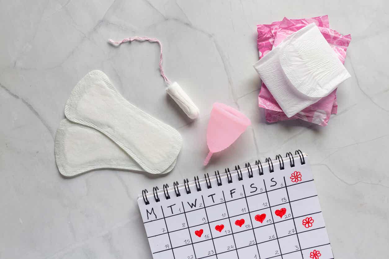 A calendar and various feminine hygiene produduts, including pads, pantyliners, a tampon, and a menstrual cup.