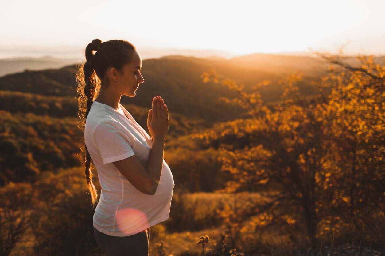 A pregnant woman meditating in nature at sunset.