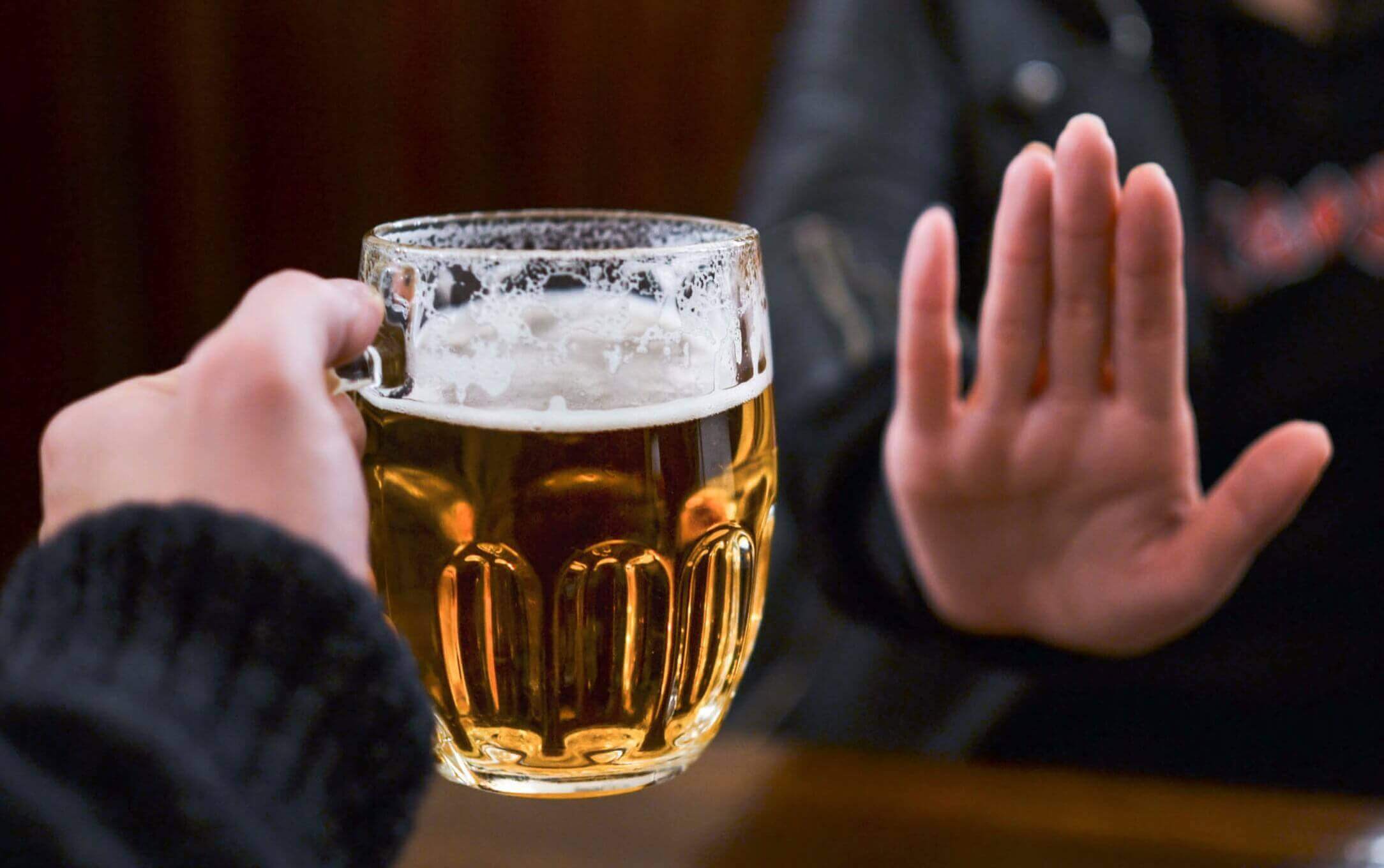 A woman turning down a glass of beer.