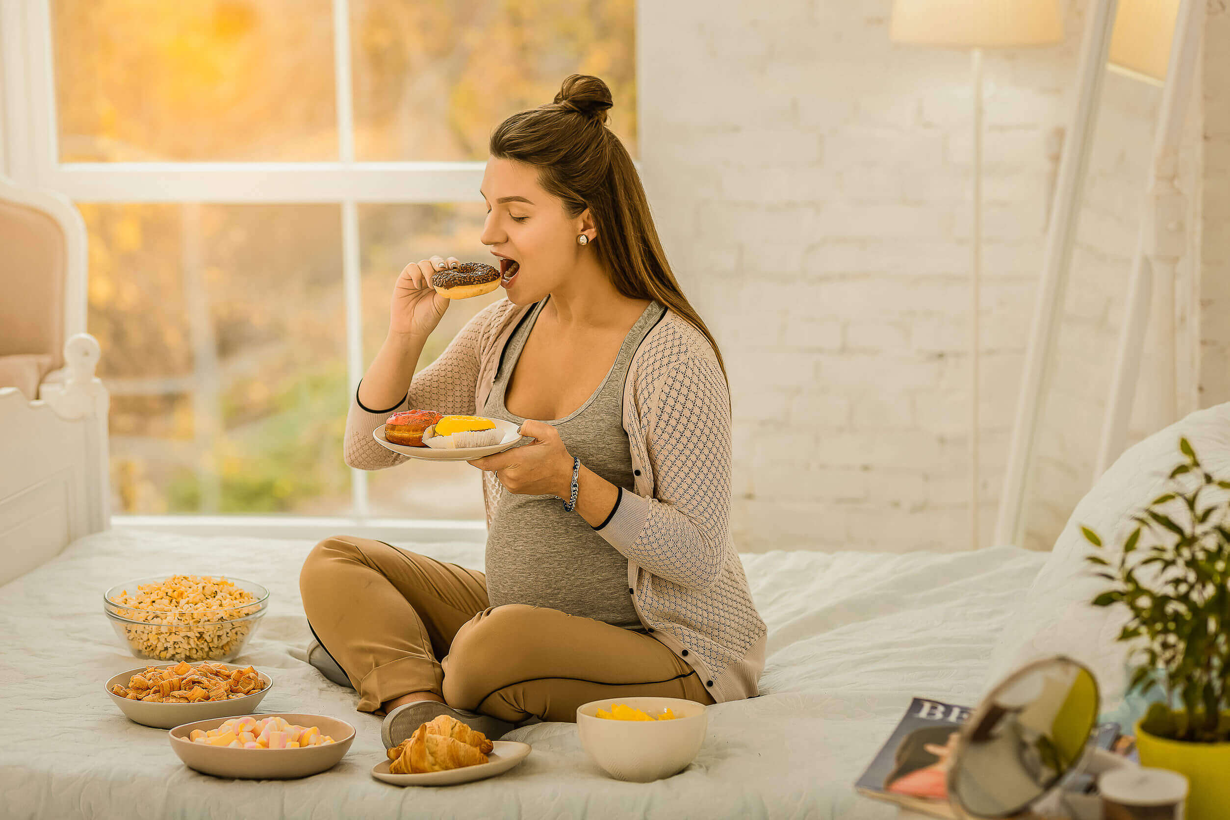 A pregnant woman witting in bed eating sweets.