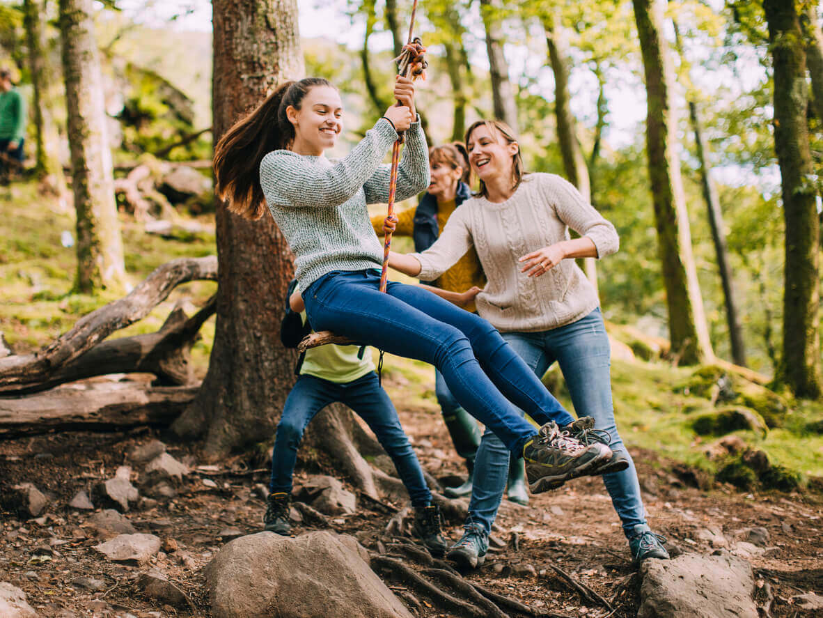 Teenagers playing on a rope swing in the woods.