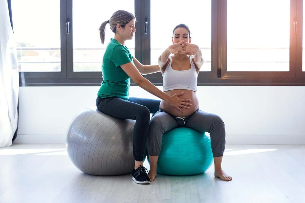 En gravid kvinne som sitter på en fitball sammen med en instruktør.