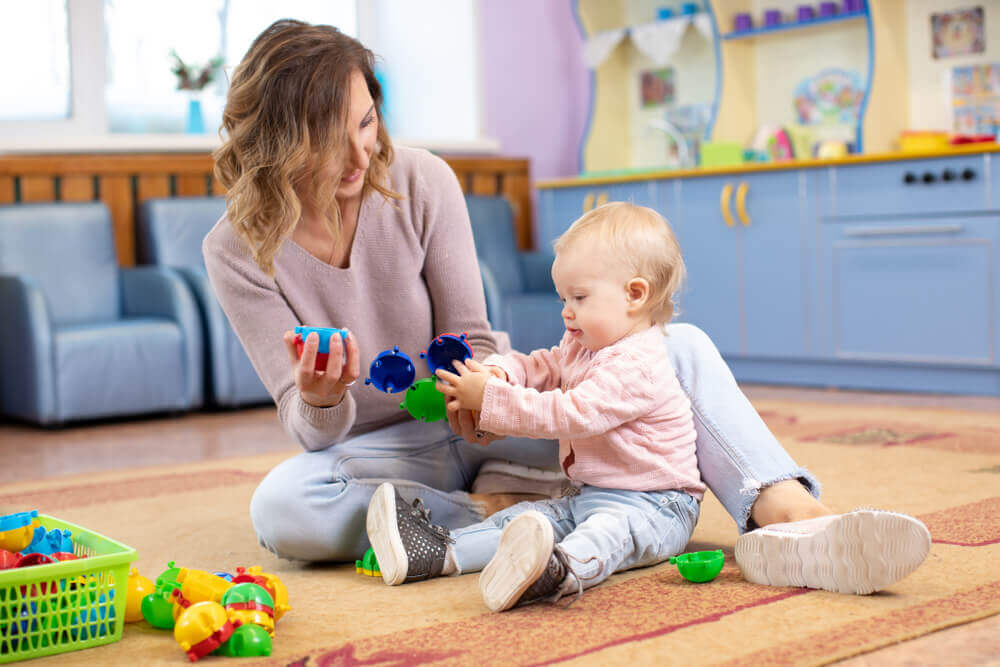 A mother sitting on the floor playing with her baby girl.