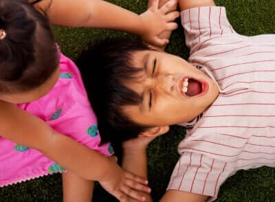 A young boy lying on the ground covering his ears.
