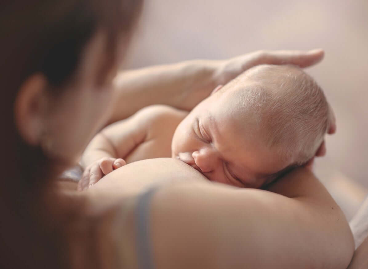 En mamma vaggar sitt barns huvud medan han ammar.