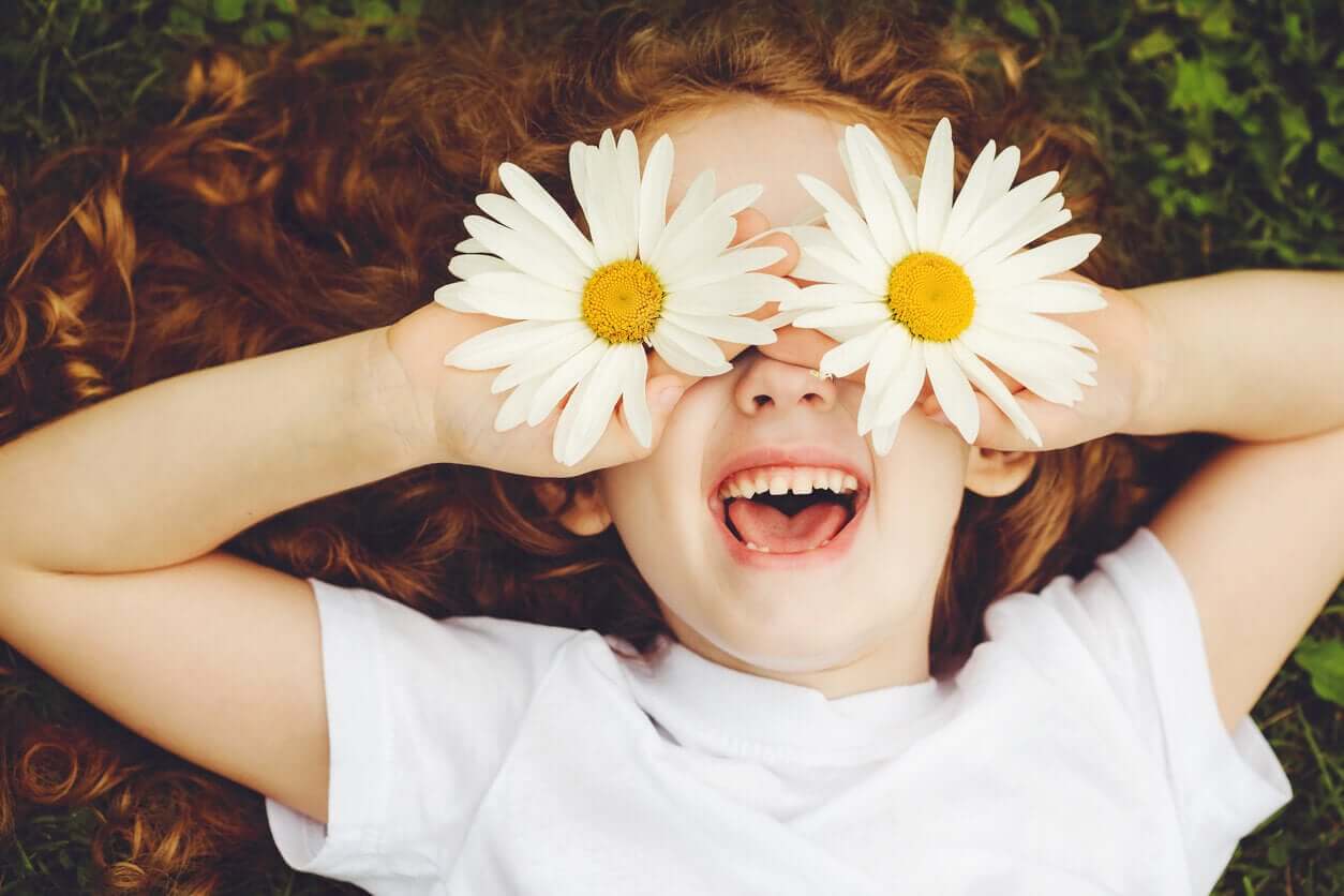 A red-headed girl holding daisies over her eyes and smiling.