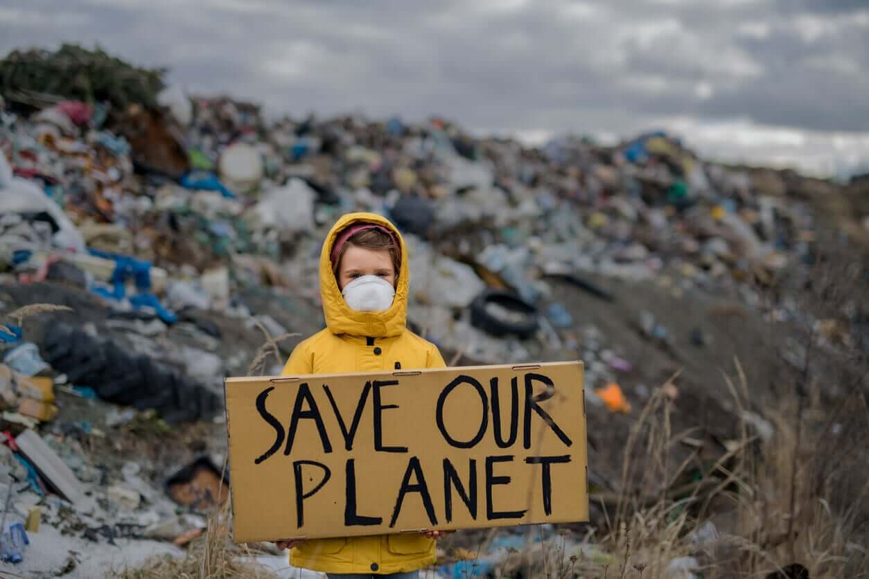 A child standing in front of a beach full of trash holding a sign that reads "save our planet".