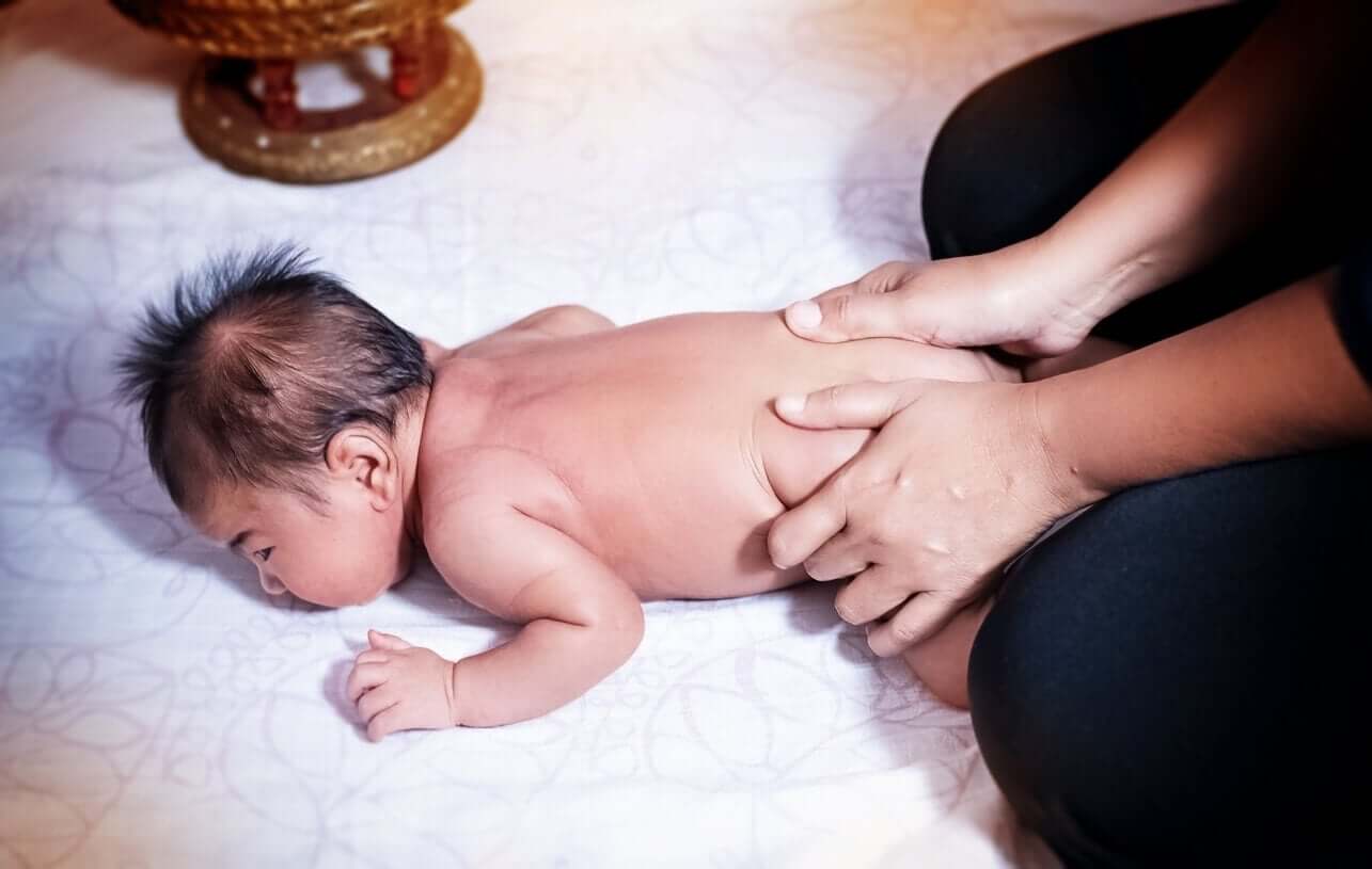 En kvinne som masserer en baby som ligger med ansiktet ned.