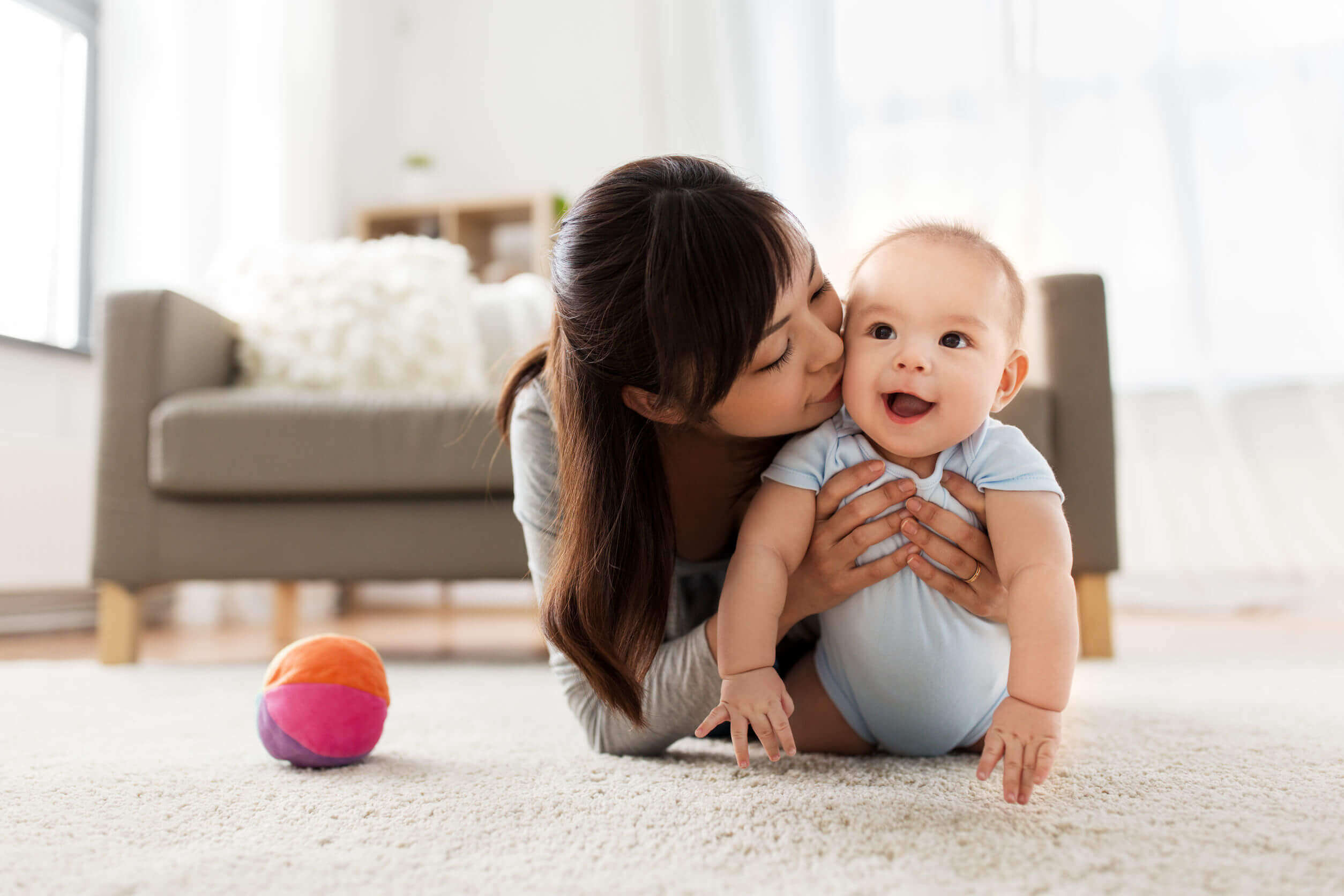 A mother lying on the floor playing with her baby.