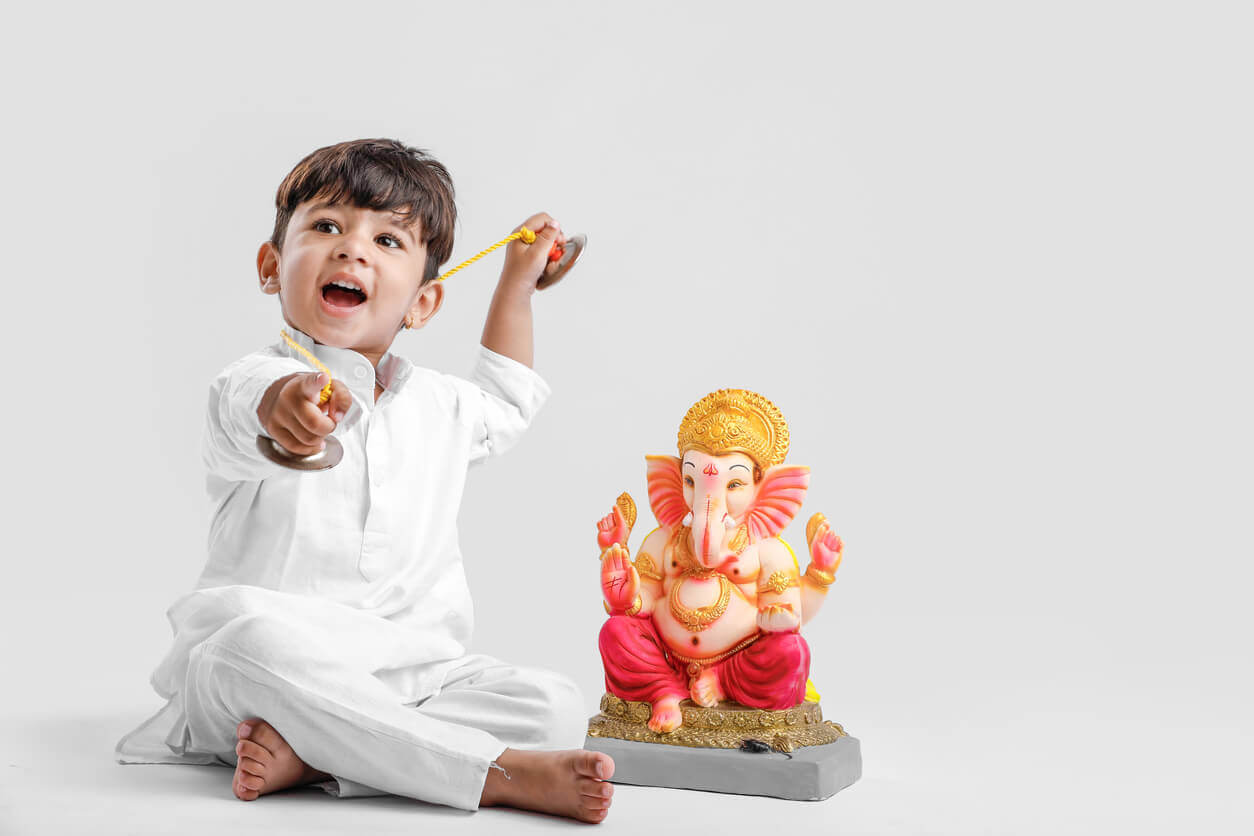 A Hindu child sitting by the statue of a Hindu god.