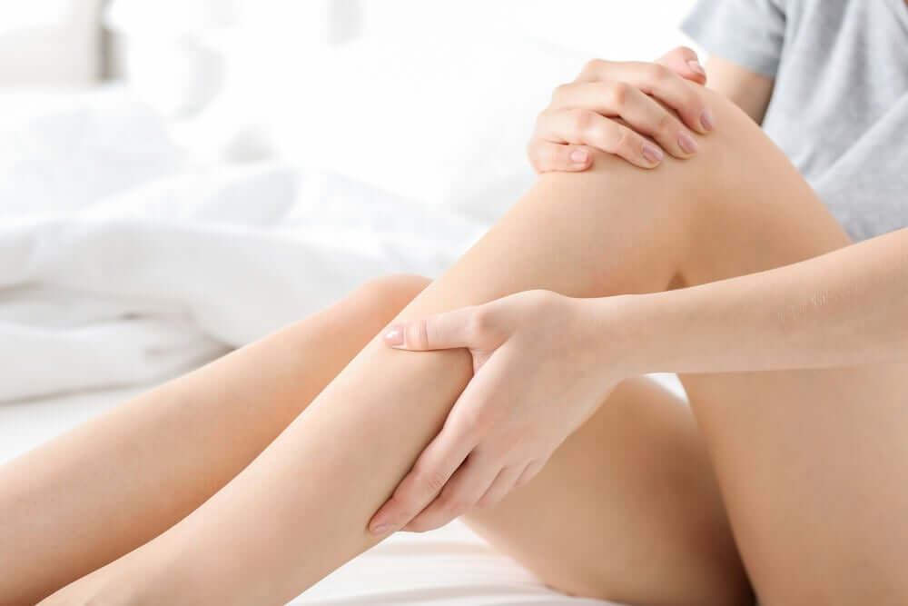 A woman sitting in bed rubbing her legs.