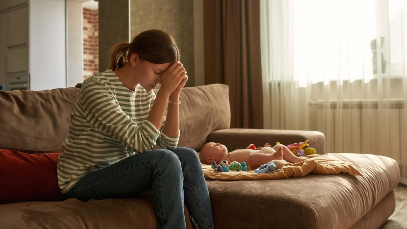 A mother looking distressed while sitting near her baby.