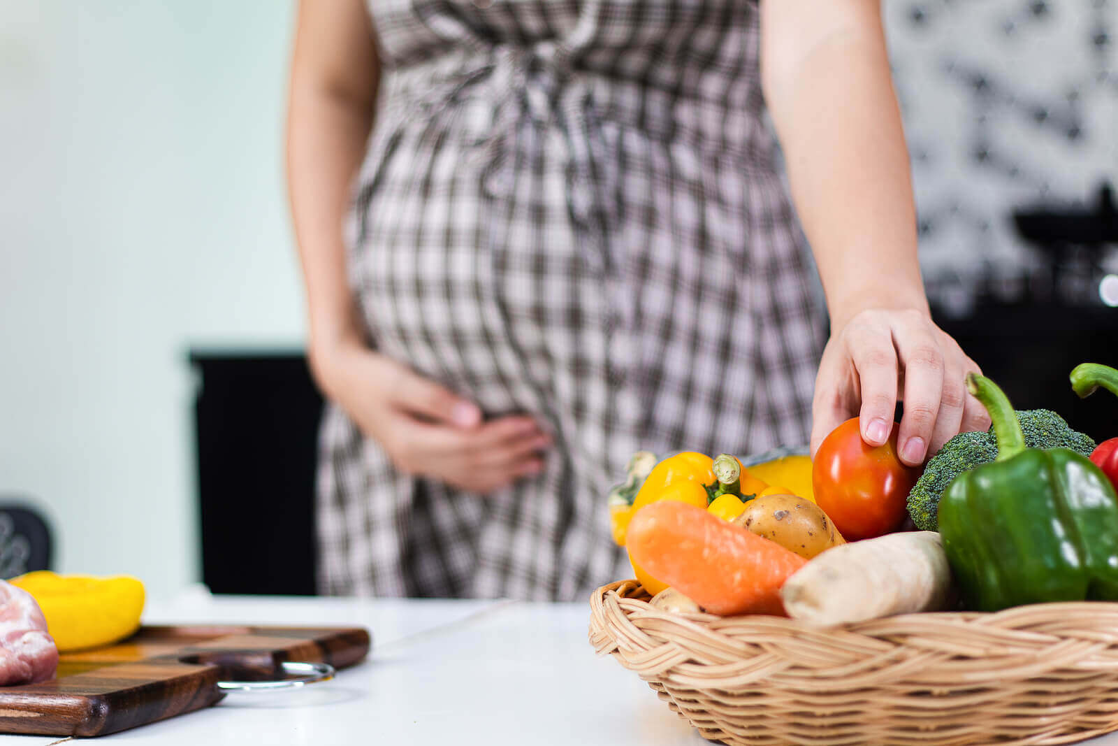 A pregnant woman grabbing a tomato from a basket of vegetables.