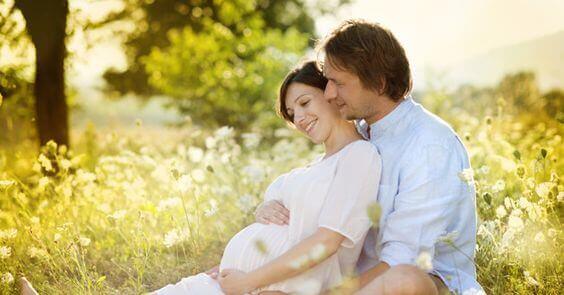 A pregnant couple sitting in a field at dawn.