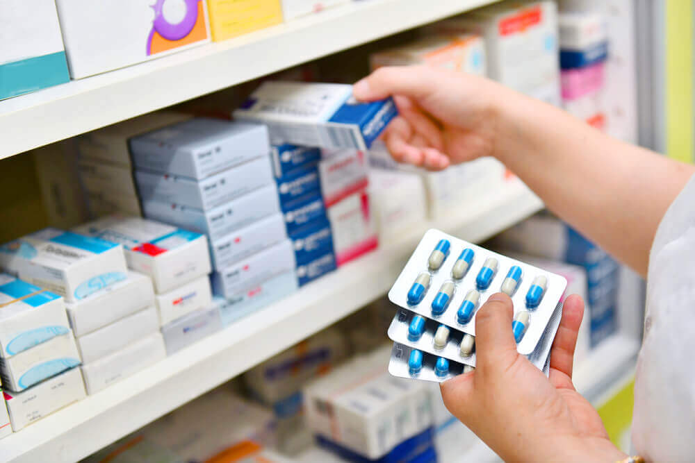 A woman stocking a shelf with medication in a pharmacy.