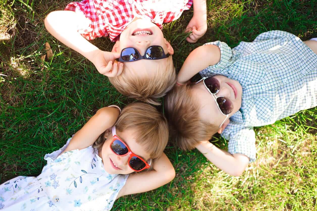 Three small children lying on the ground wearing sunglasses.