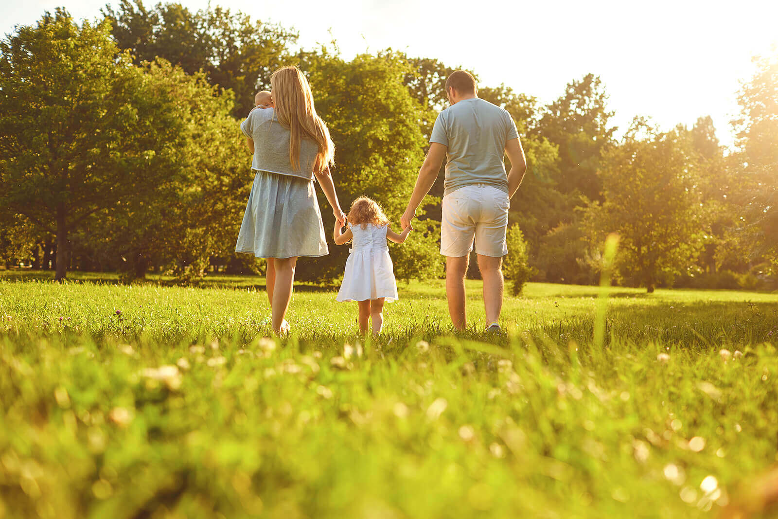 Parents walking with their young children in a field on a sunny day.