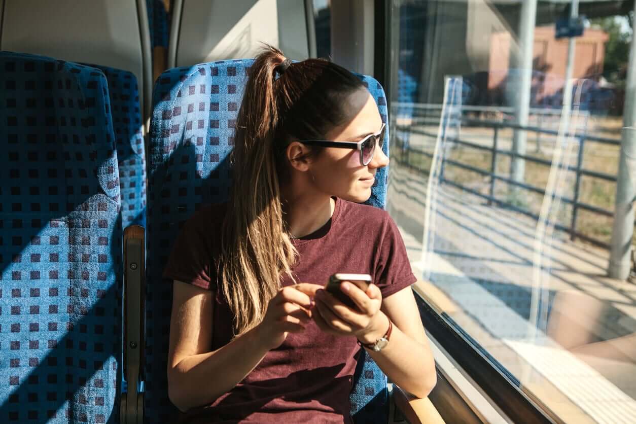 A teen girl riding on a train and using her smart phone.