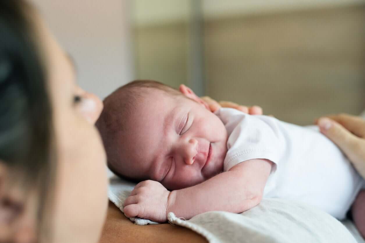 A woman holding a sleeping smiling newborn on her chest.